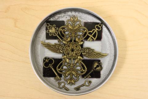 Metal mason jar lid filled with metal gears, and black and white tiles.