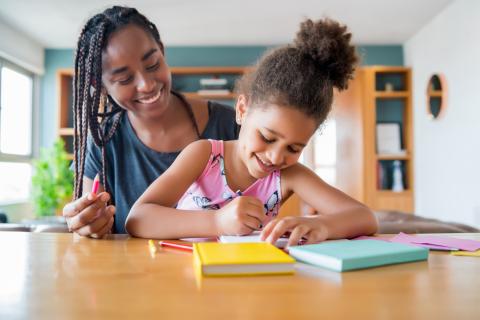 a mother helping a child with writing while sitting at a table
