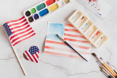 A watercolor picture of an American flag with paints and paintbrushes