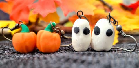 Two pairs of earrings made of polymer clay, one set in the shape of pumpkins and the other in the shape of ghosts.