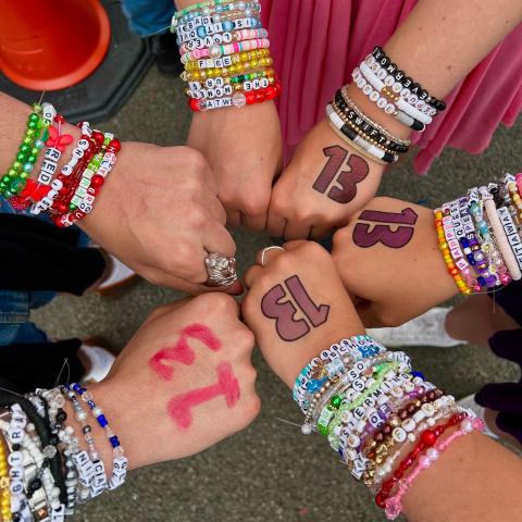 6 fists in a circle, their writs bearing several bead bracelets and the number 13 written on the backs of their hands