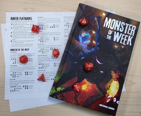 A Monster of the Week handbook, Monster Hunter profiles page, and a set of red polyhedral dice. 