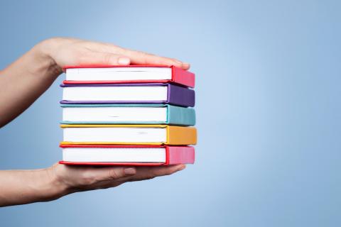 A pair of hands holding a stack of colorful books between them.
