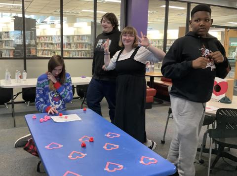 table with pink and red rubber ducks and paper hearts surround be 4 teens