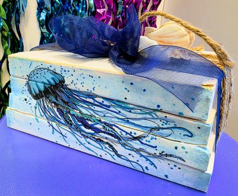 A stack of three books have been glued together, an image of a jellyfish has been applied to the spine and colored in, and there is twine and ribbon with shells around the books for a decorative shelf piece.