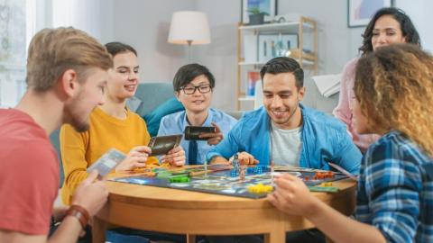 diverse group of guys and girls playing in a strategic board game with cards and dice cozy living room in a daytime
