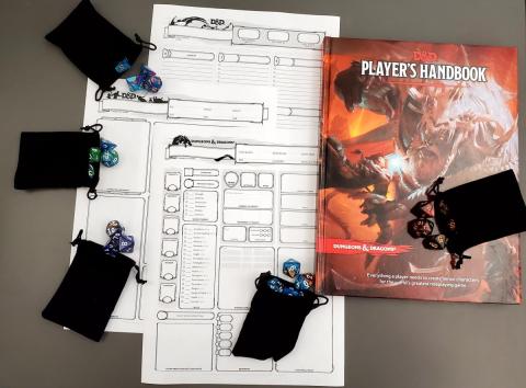 A Dungeons and Dragons player's handbook sits next to a template character sheet as well as black pouches of tabletop gaming dice sets.
