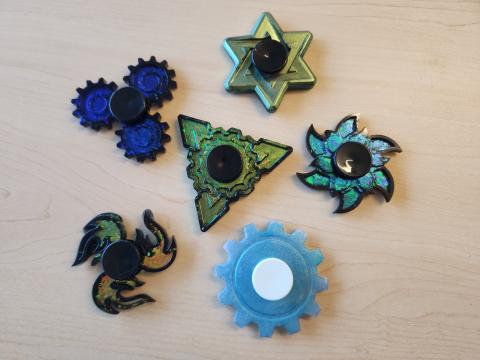 Samples of fidget spinners made out of resin and colored mica flakes or powder in shapes of gears, star, triangle, flames, and flower