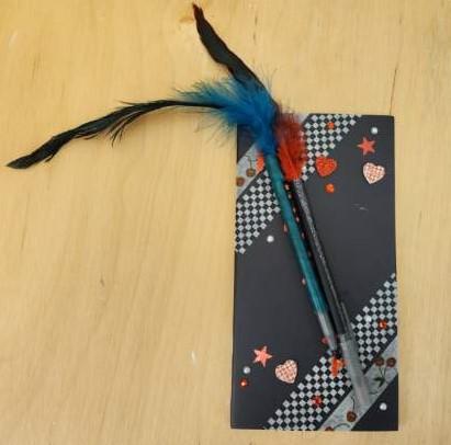 Black planner decorated with pale washi tape, heart stickers, and feathered pens