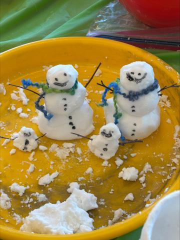Four snowman made from artificial snow on a yellow tray decorated with branches and yarn