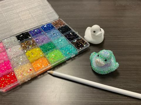 Bedazzle beads in a tray, tool, a white duck for decorating, and a duck cover in bedazzle beads