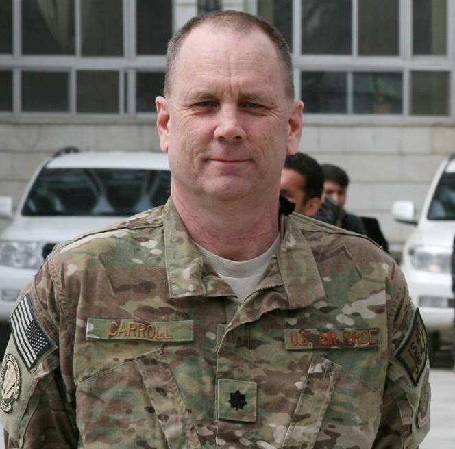 Older adult man wearing camouflage uniform faces forward