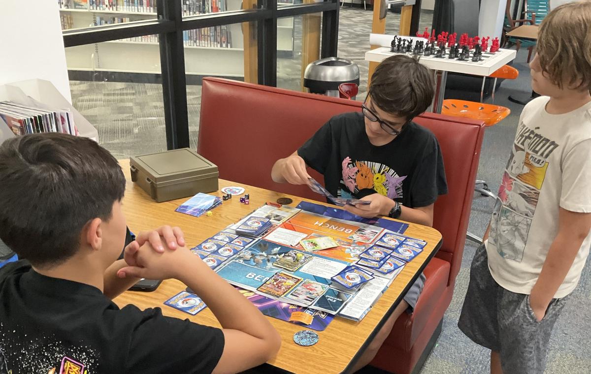 Three teen boys playing the Pokemon card game.