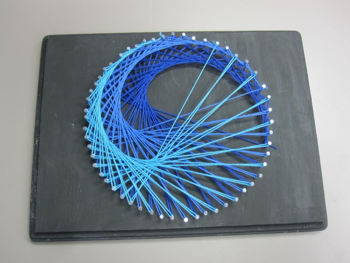 Three shades of blue threads stringed across nails in round shape on a black board