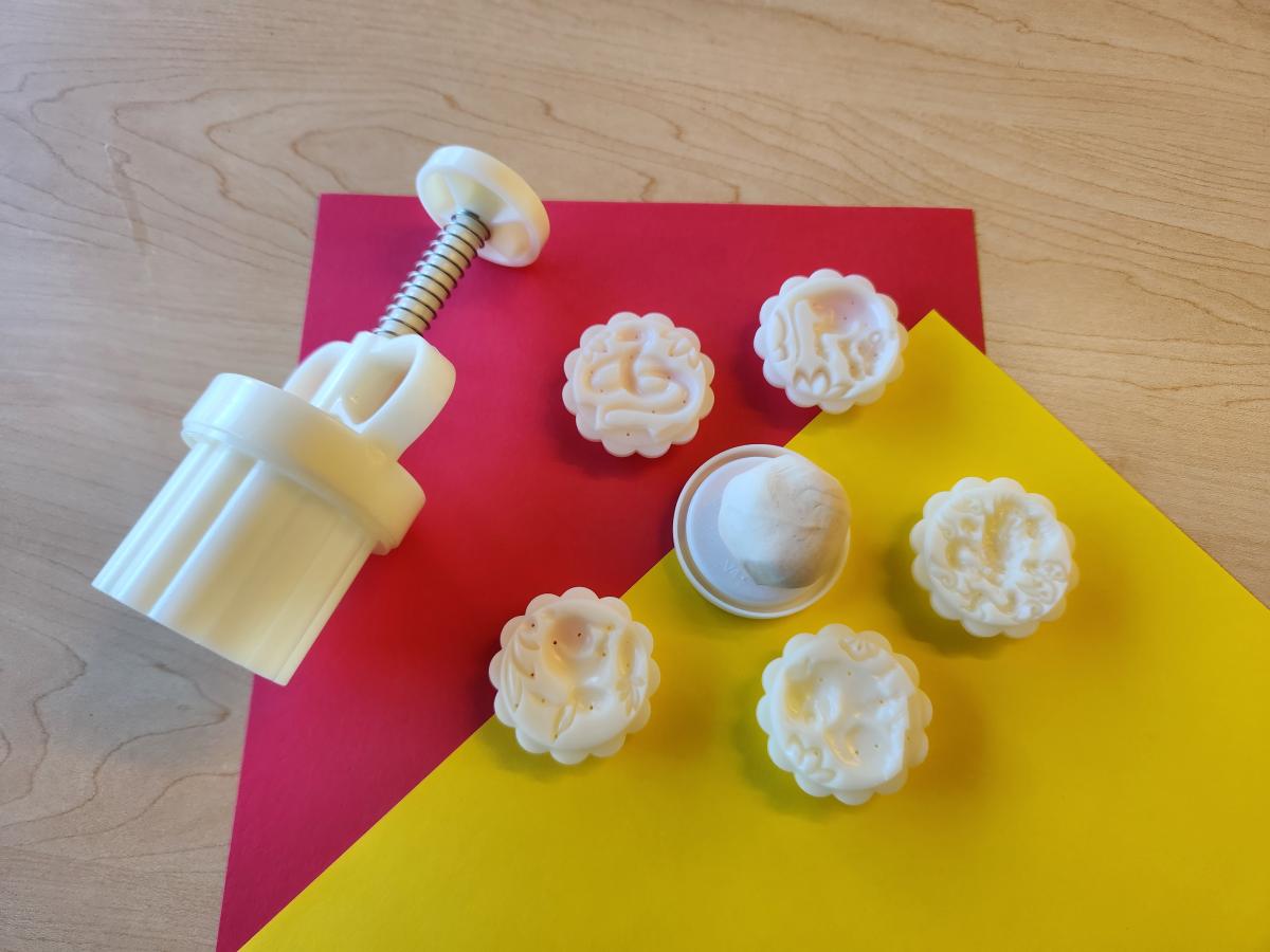 Mooncake mold with a couple molds and clay on red and yellow paper.