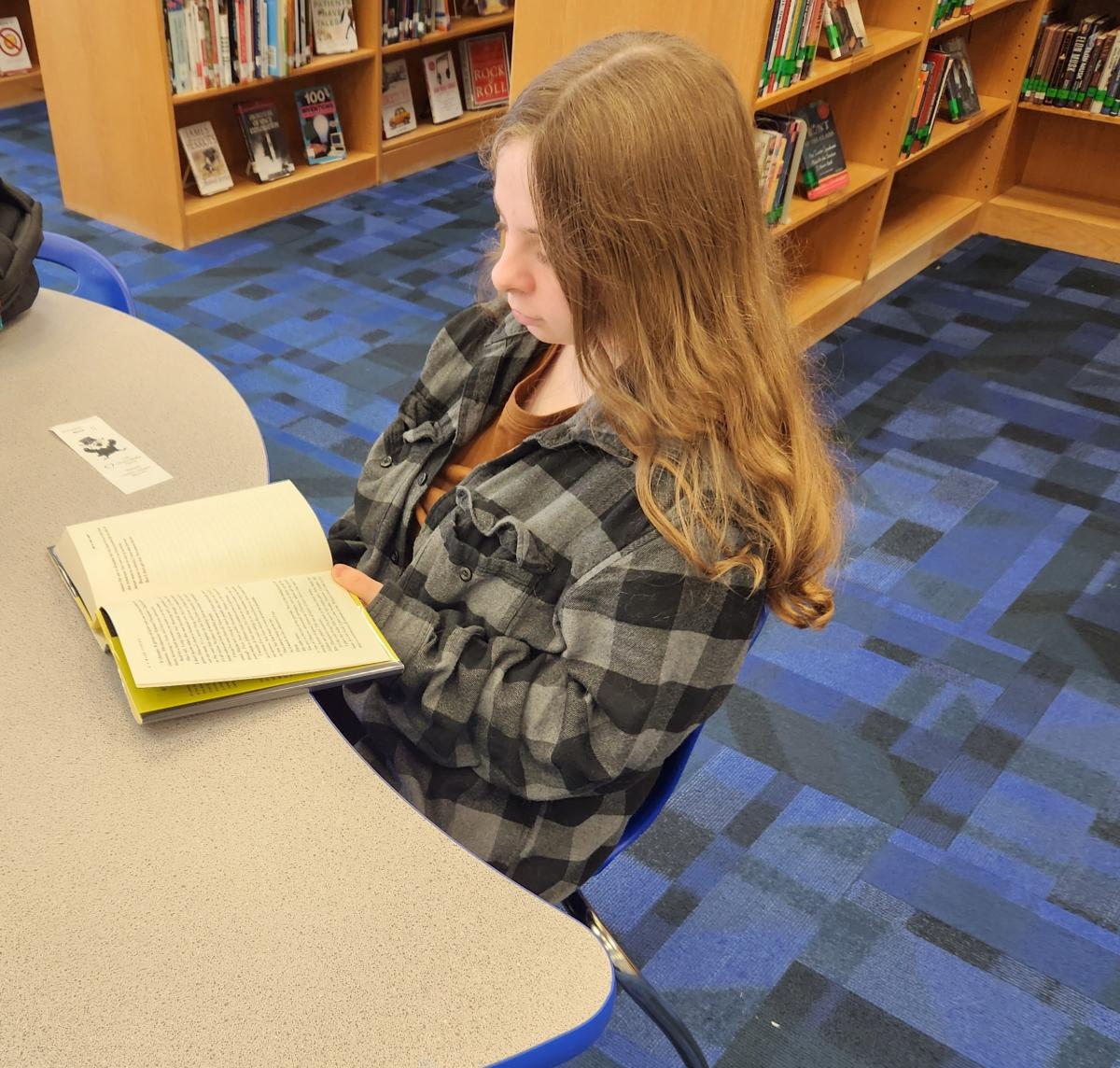 A girl at a table reading a book.