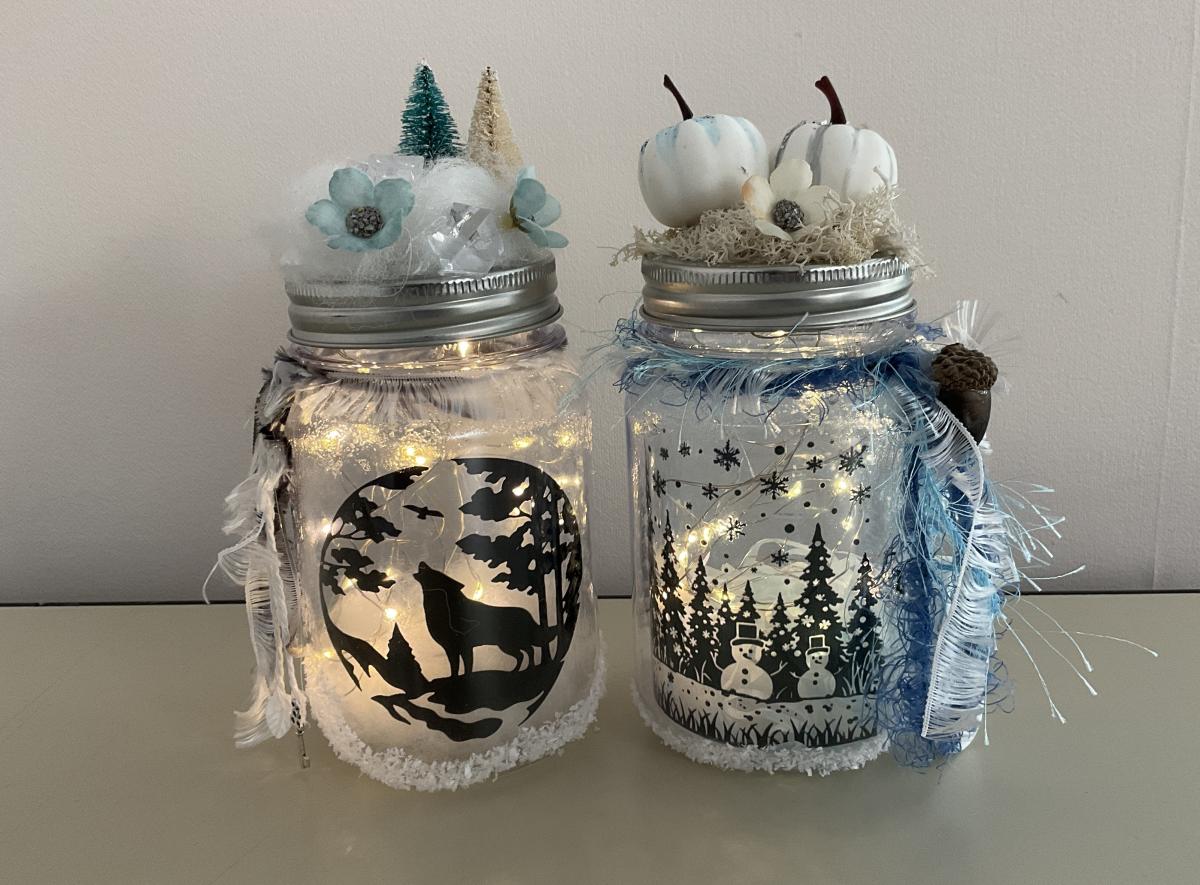 2 mason jars with winter themed silhouettes, fairy lights, and winter themed decorations