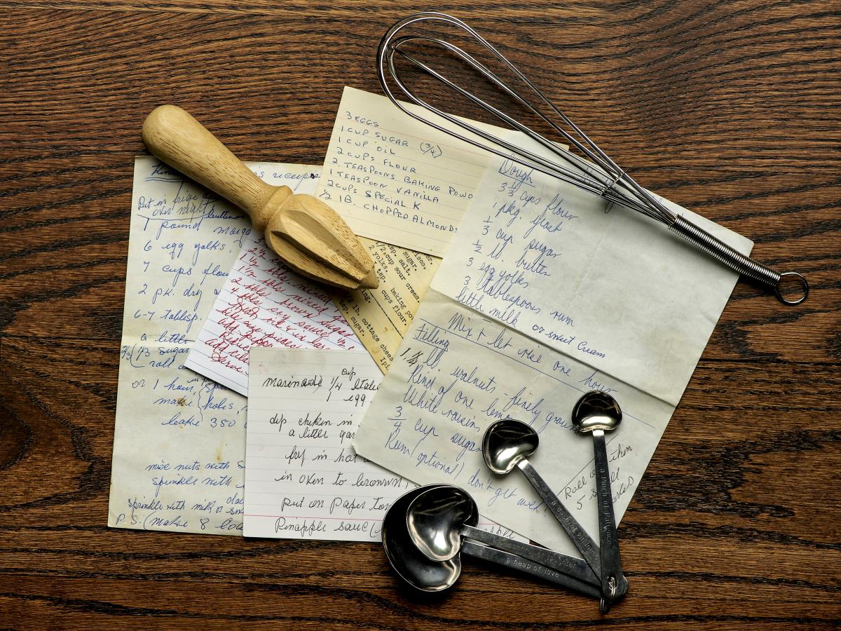 Several old recipes with measuring spoons and a whisk on a table.